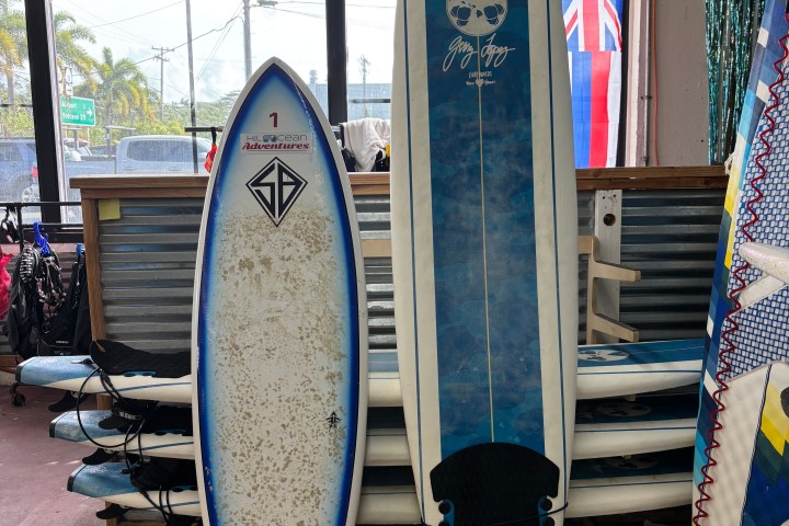 Two surfboards standing upright in a shop with a Hawaiian flag in the background.