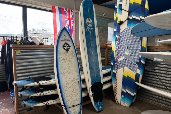 Three surfboards leaning on a wall, next to a window and a Hawaiian flag indoors.
