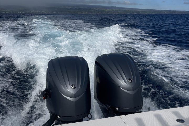 Two boat engines with ocean wake and cloudy sky in background.
