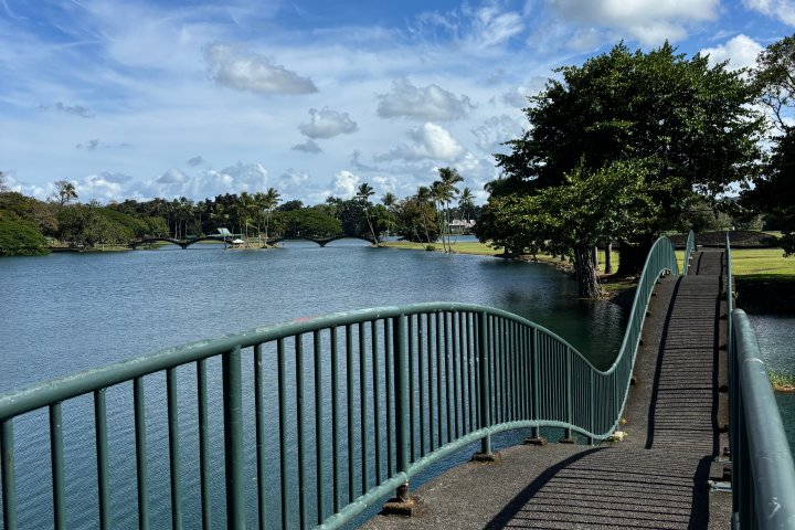 Curved bridge over water with green railing under a blue sky with clouds.