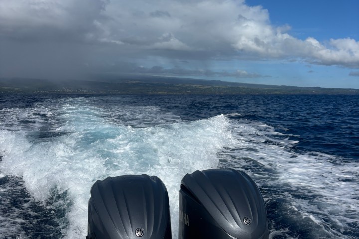 Twin boat engines on water leaving a white wake under a blue sky.