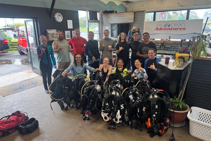 Group of 15 people posing with diving gear inside a dive shop.