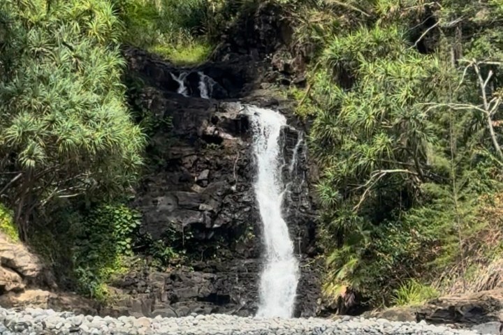 Waterfall cascading over rocks surrounded by lush greenery into a blue pool.