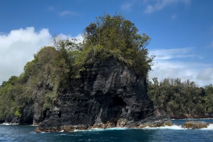 Rocky island with lush vegetation surrounded by ocean under a blue sky.