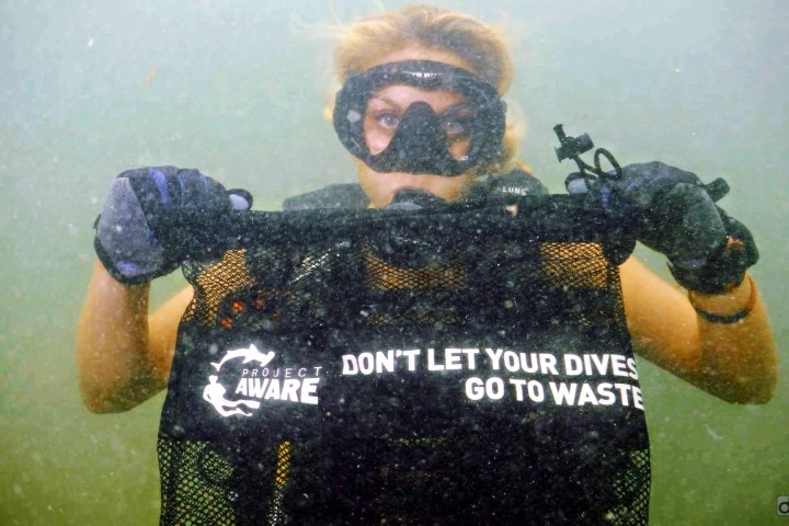 Underwater diver holds net bag with 'Project AWARE' and slogan 'Don't let your dives go to waste.'