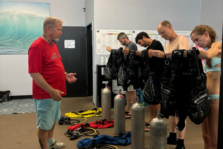Diving instructor teaching a group about scuba gear in a classroom setting.