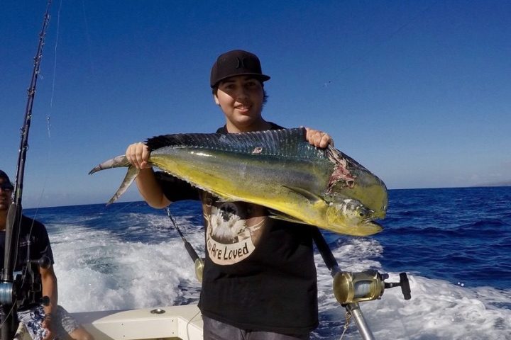 Person holding a large fish on a boat in the ocean under a clear blue sky.