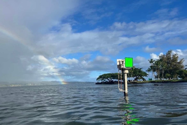 Water view with a rainbow, sky, and a marker pole in the foreground.