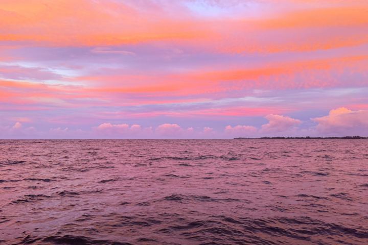 Vibrant pink and orange sunset over the ocean with clouds in the distance.