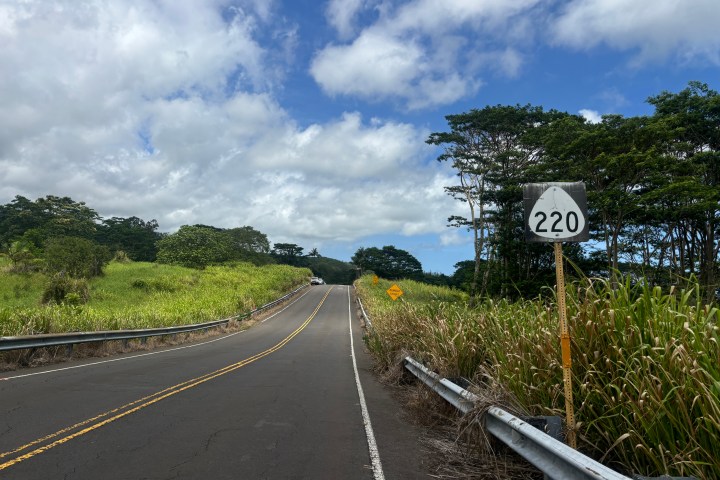 Rural road with Route 220 sign, bordered by grass and trees under a cloudy sky.