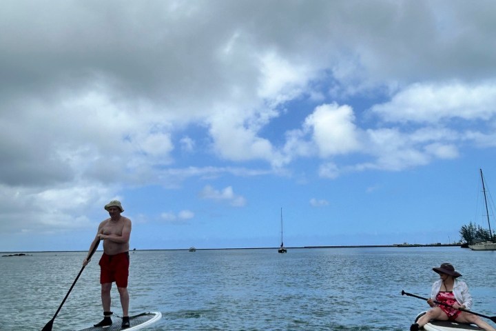 Two people paddleboarding on calm sea under a cloudy sky.