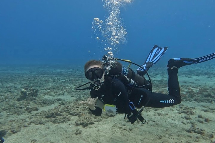 Scuba diver underwater in ocean, making a hand gesture, with bubbles rising.