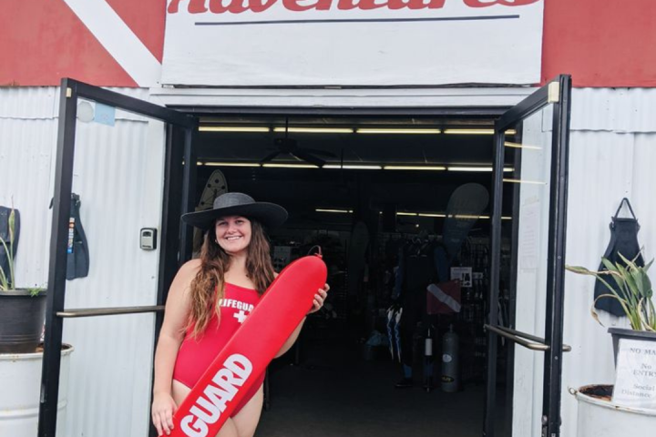 Person in a lifeguard suit holding a buoy at an adventure store entrance.