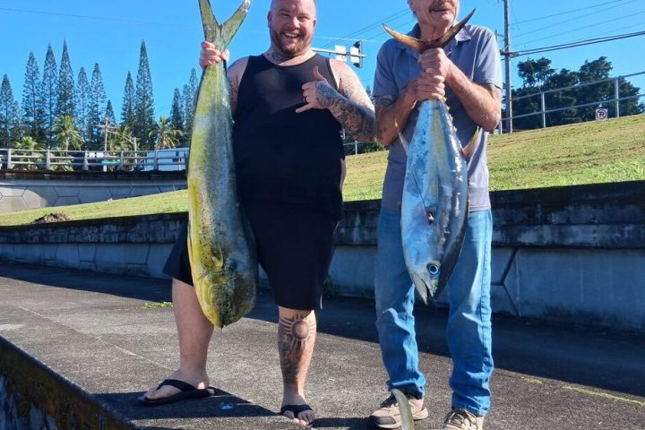 Two men holding large fish on a concrete platform near a road.