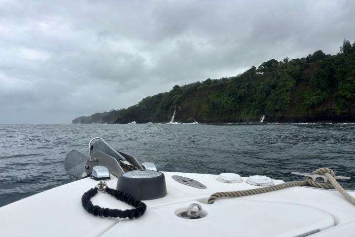 Boat on ocean with cloudy sky and distant green cliffs.
