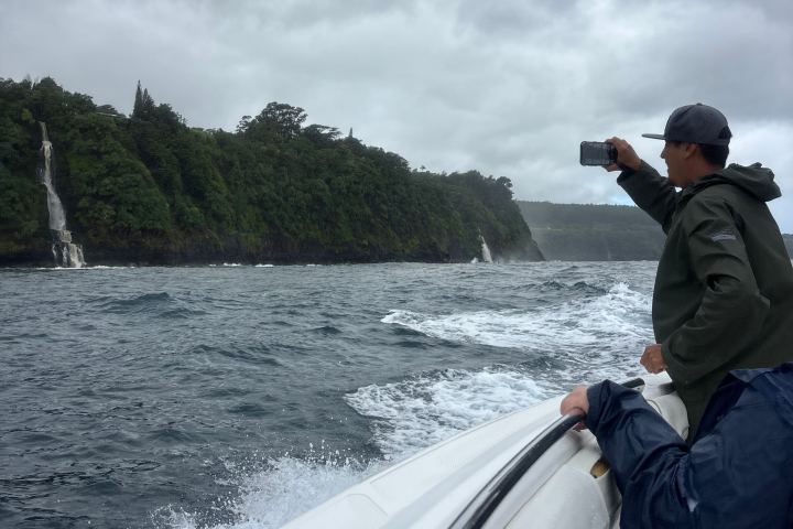 People on a boat near a coastal waterfall with cloudy skies.